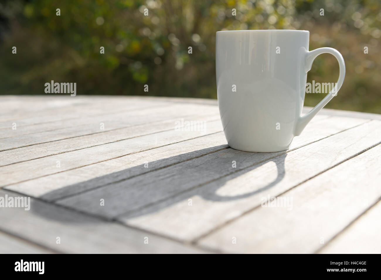 Bianco di ceramica bicchiere su un disco un tavolo di legno sotto la luce diretta del sole Foto Stock