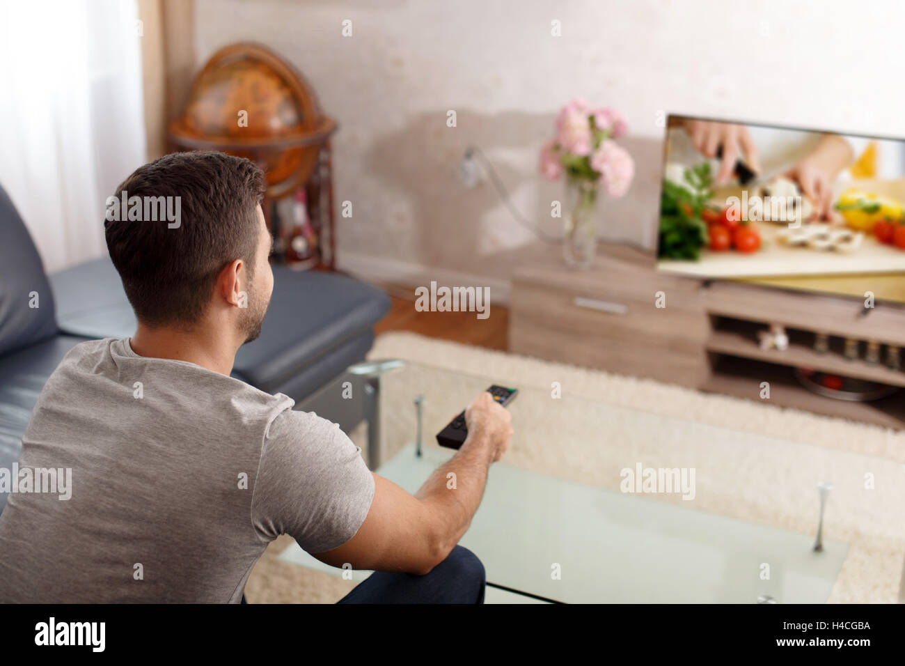 Uomo eccitato guardando la cottura di tutorial in TV, spingendo il pulsante sul telecomando Foto Stock