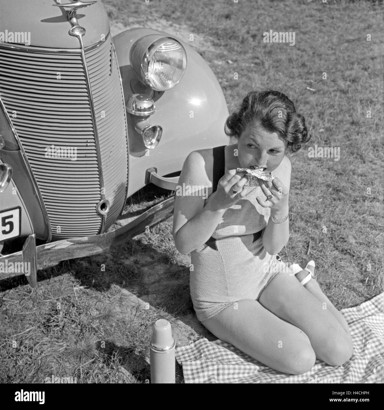 Eine Frau beim Picknick vor einem Ford V6, Deutschland 1930er Jahre. Una giovane donna avente un pick nick nella parte anteriore di una Ford V8, Germania 1930s. Foto Stock