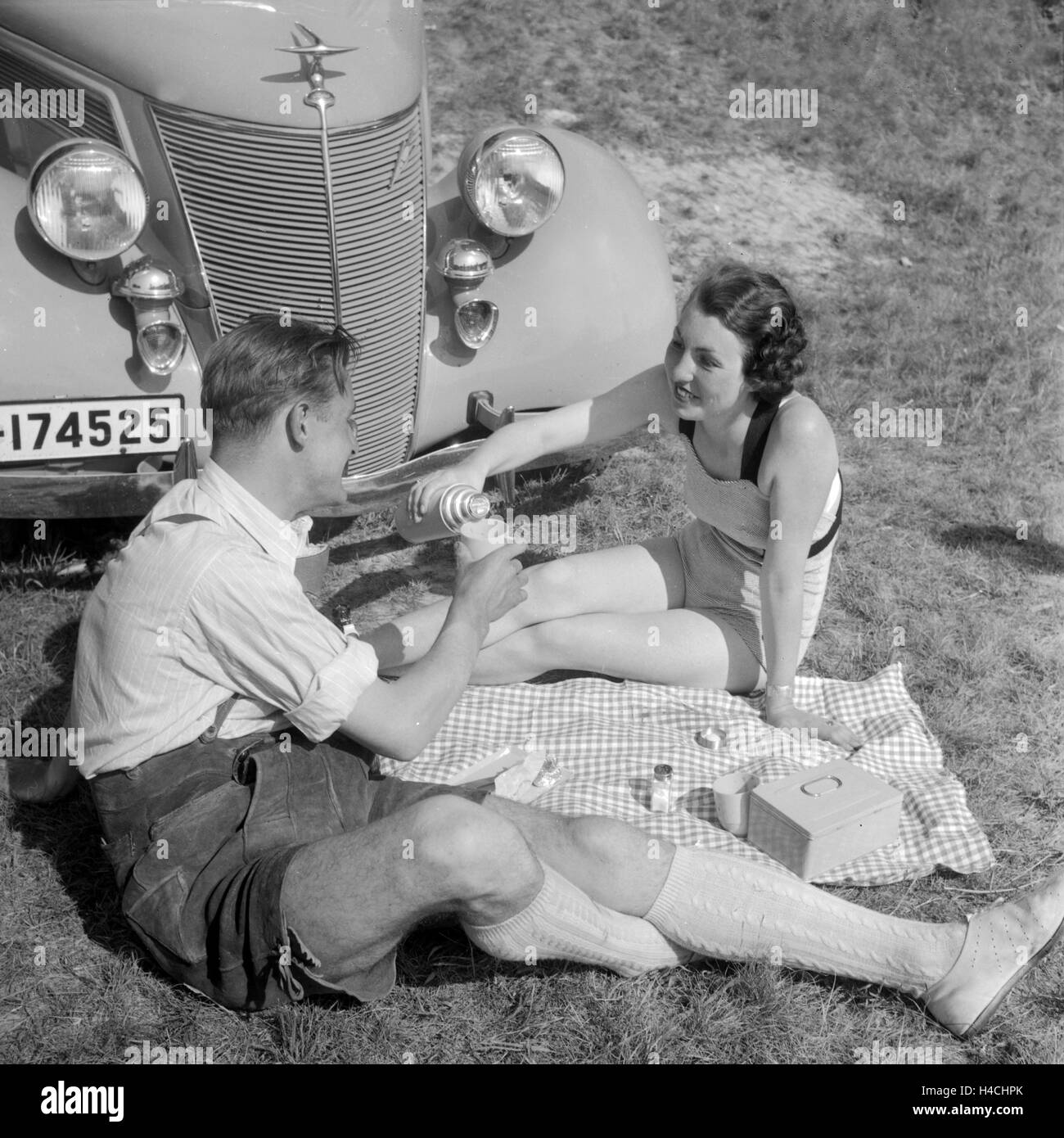 Ein junges Paar beim Picknick vor einem Ford V6, Deutschland 1930er Jahre. Una giovane coppia avente un pick nick nella parte anteriore di una Ford V8, Germania 1930s. Foto Stock