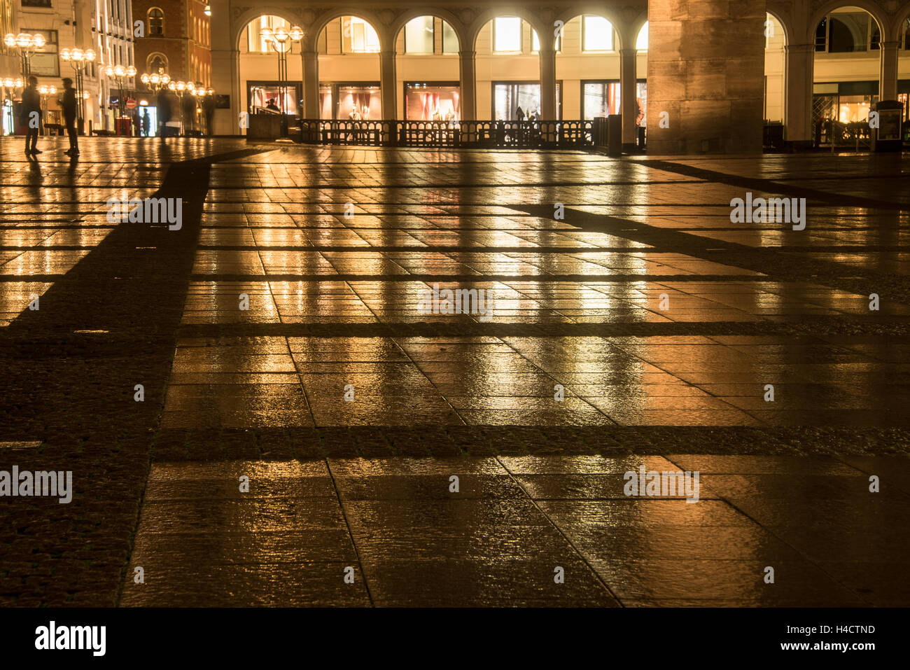 Vista sulla grande piazza bagnato nella città riflettendo edifici illuminati in una notte piovosa Foto Stock