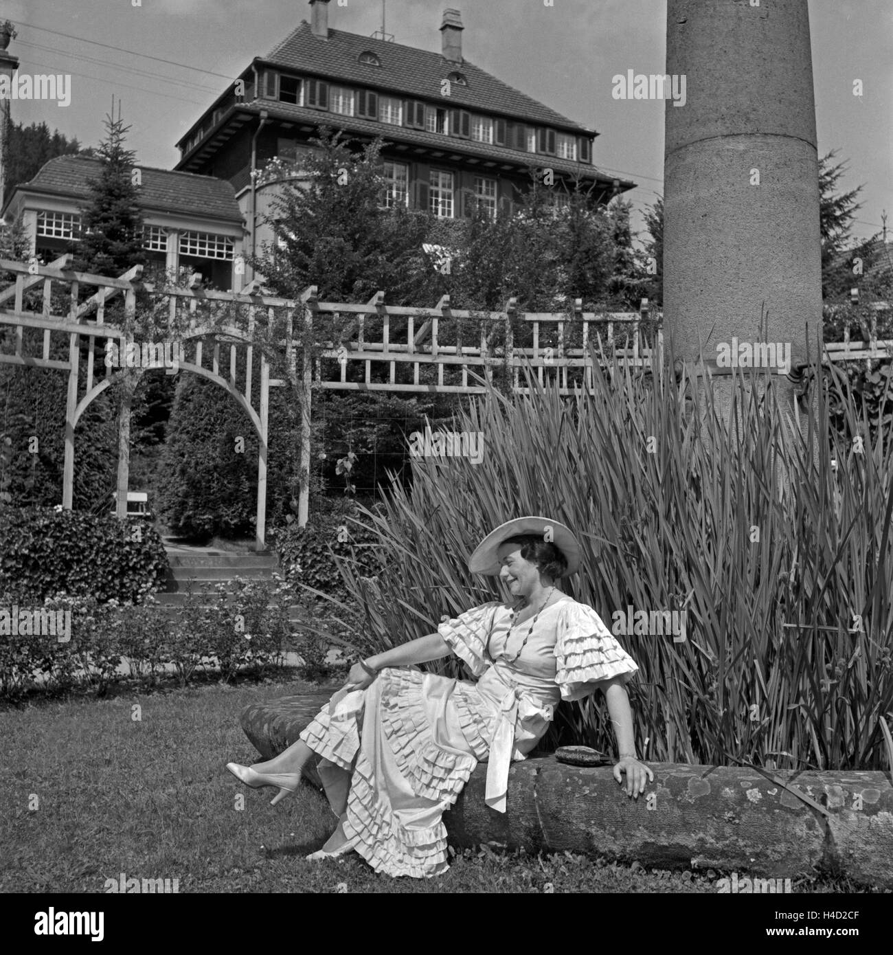 Eine Frau in einem bodenlangen weißen Kleid sitzt im Garten eines Kurhotels in Wildbad im Schwarzwald, Deutschland 1930er Jahre. Una donna in un lungo abito bianco seduti nel giardino di un resort termale a Wildbad nella Foresta Nera, Germania 1930s. Foto Stock