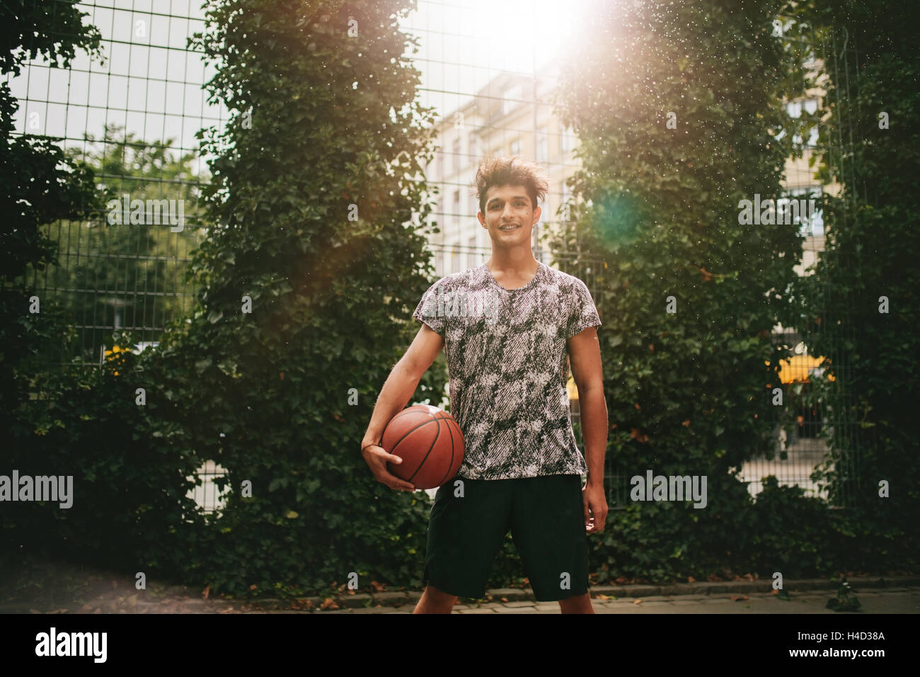 Ritratto di giovane uomo con una palla da basket sulla corte esterna. Sorridente teenage streetball player guardando la fotocamera. Foto Stock