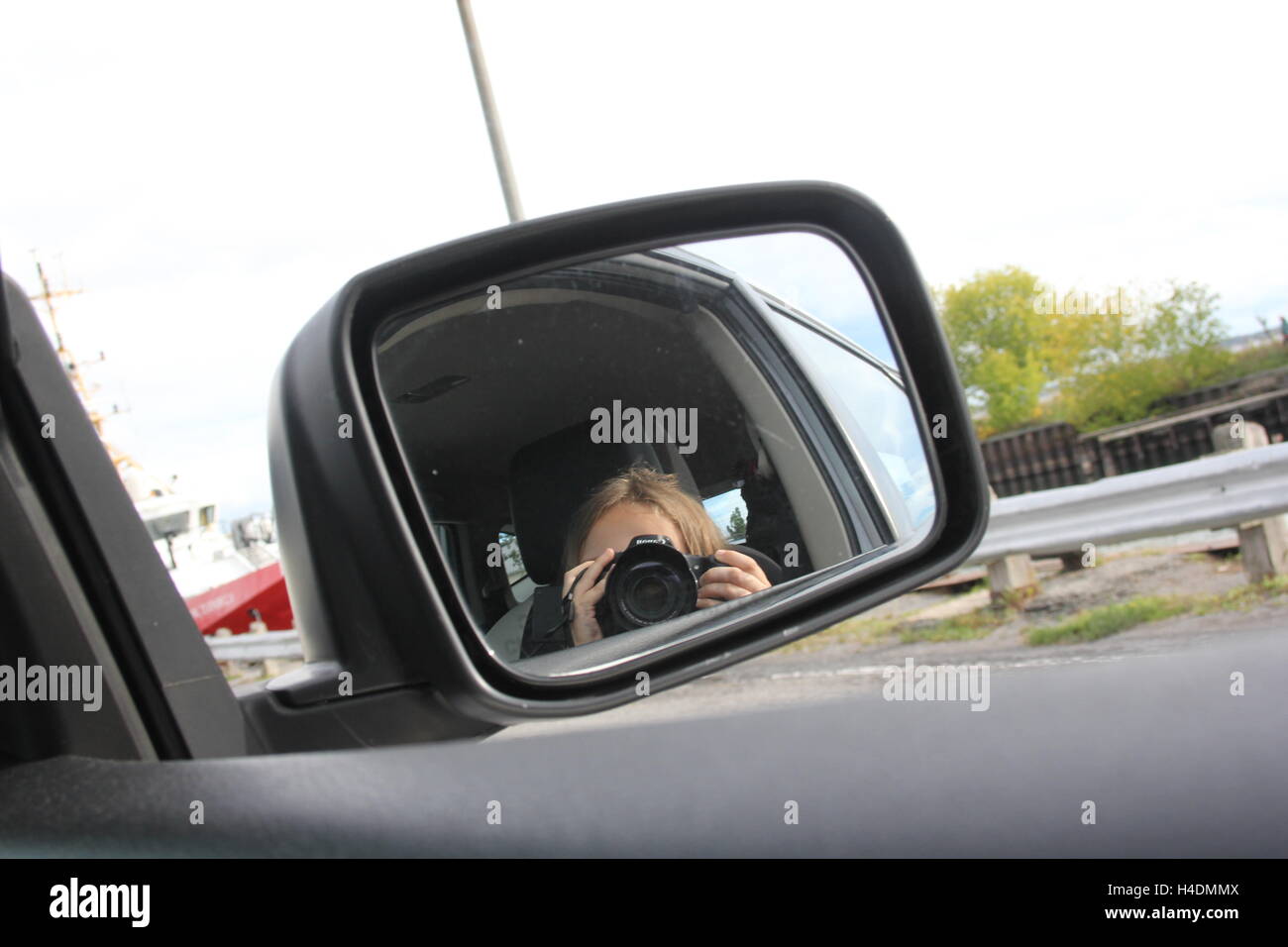 Ragazzina tenta di prendere un selfie in uno specchio laterale di una automobile. Foto Stock