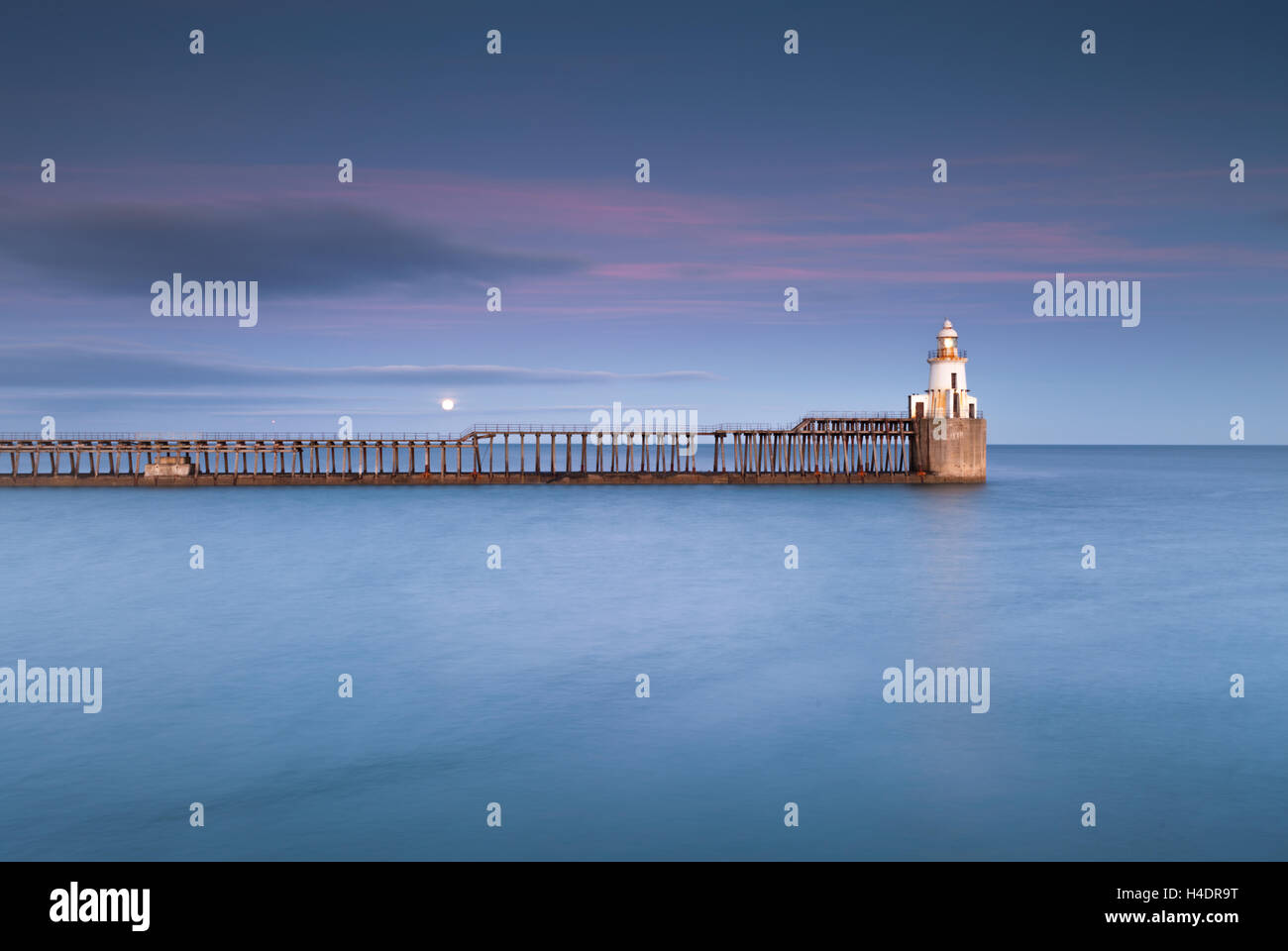 Poco bianco faro alla fine di un lungo molo di legno a Blyth porto sulla costa di Northumberland al sorgere della luna Foto Stock