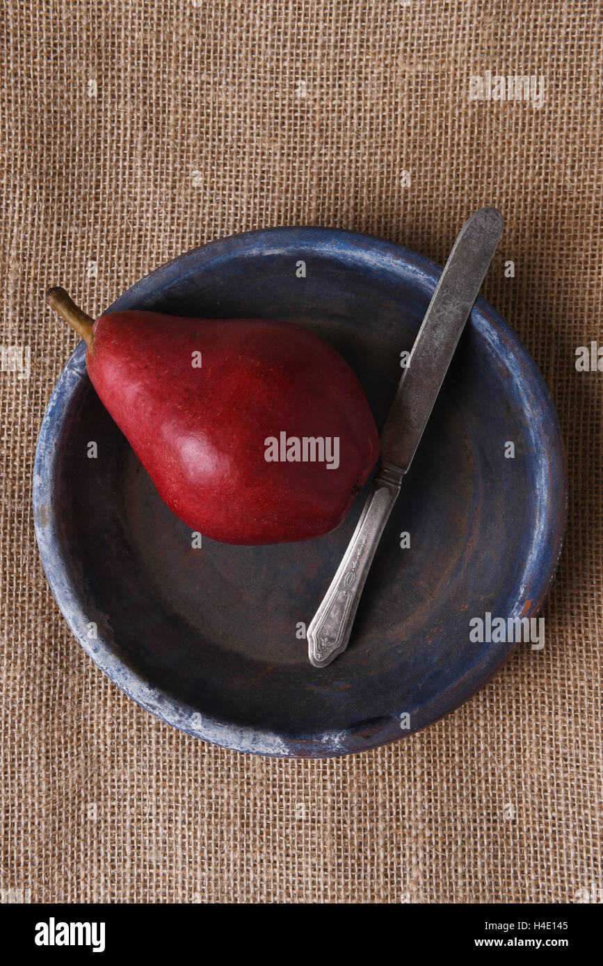 Elevato angolo di visione di un rosso pera e coltello su una piastra blu su tela. Foto Stock