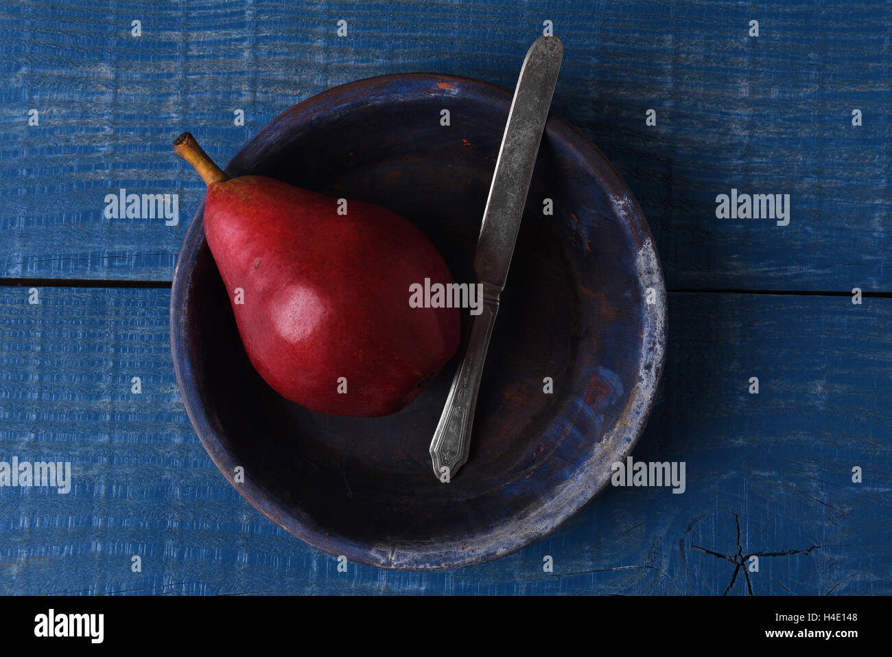 Elevato angolo di visione di un rosso pera e coltello su una piastra blu blu sulla tavola in legno rustico. Foto Stock