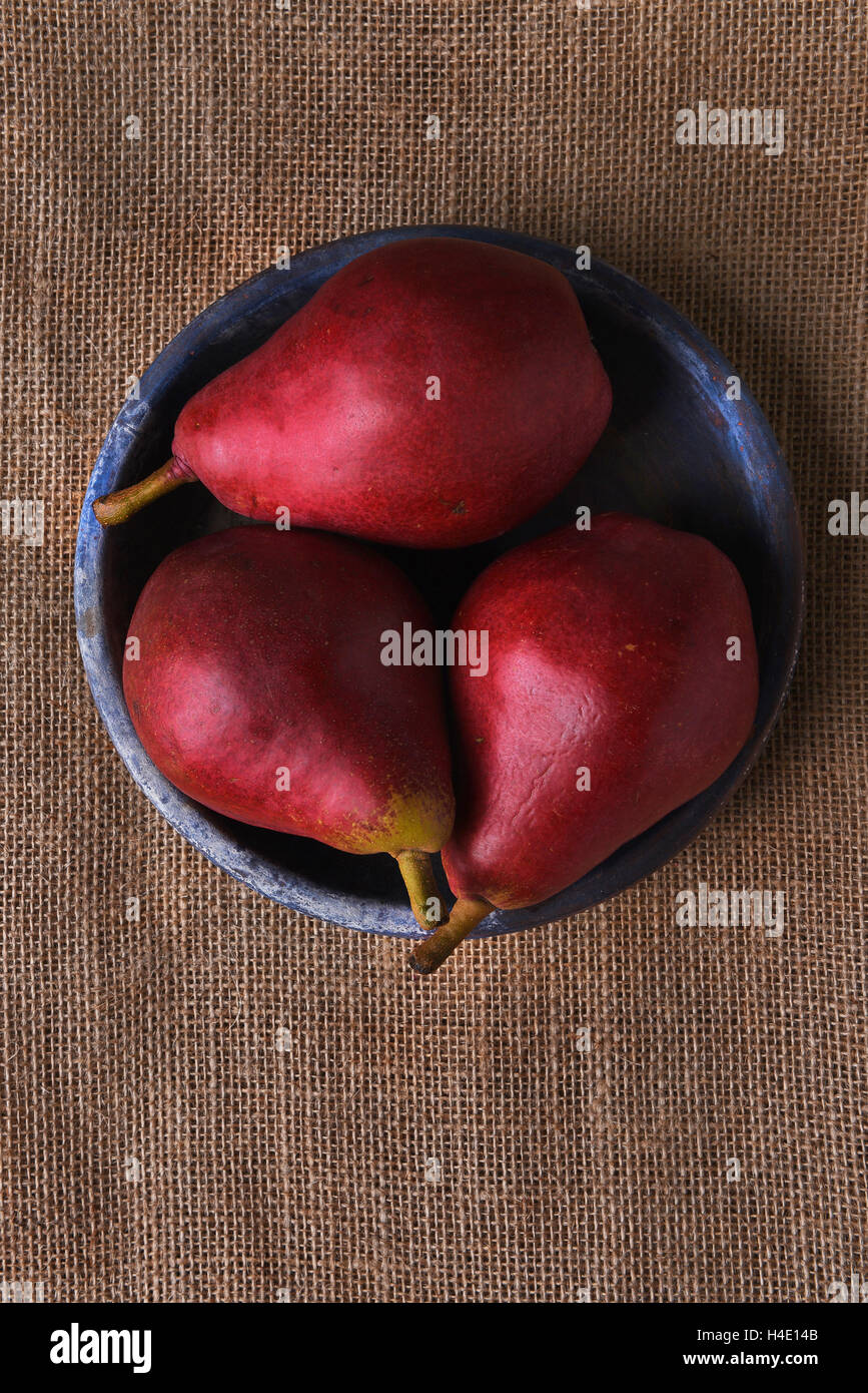 Piastra di colore blu con tre pere rosso su una tela ruvida la superficie. Formato verticale con copia spazio. Foto Stock