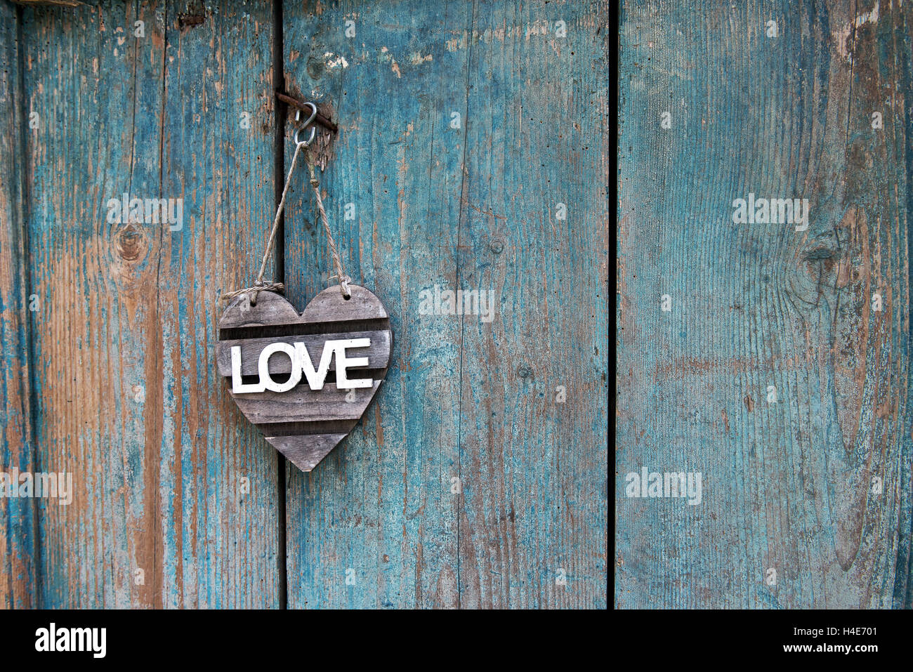 Rustico segno di amore a forma di cuore con il testo bianco appeso su un vecchio blu weathered porta in legno con spazio di copia Foto Stock