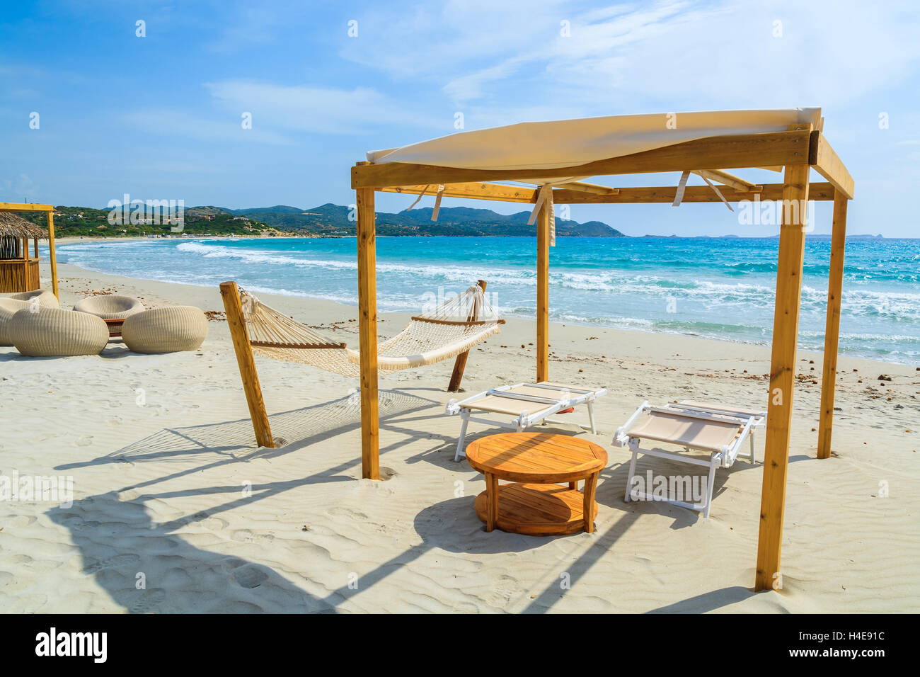 Sdraio in legno con tavolo in teak sulla spiaggia di sabbia bianca di Porto Giunco Bay, l'isola di Sardegna, Italia Foto Stock