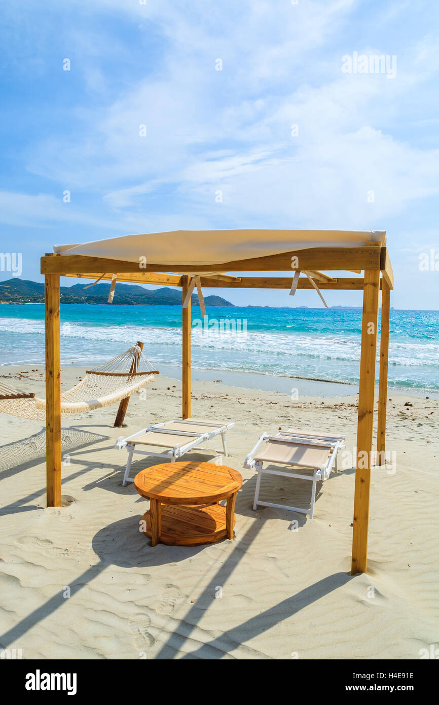 Sdraio in legno con tavolo in teak sulla spiaggia di sabbia bianca di Porto Giunco Bay, l'isola di Sardegna, Italia Foto Stock