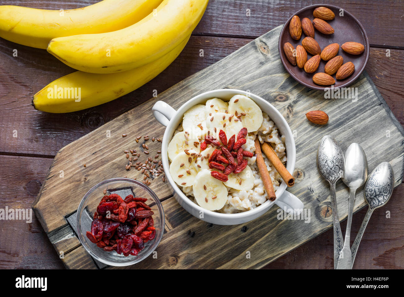Farina di avena porridge con banana, cannella, secco goji bacche e semi di lino sul tagliere di legno. Cibo sano, uno stile di vita sano Foto Stock