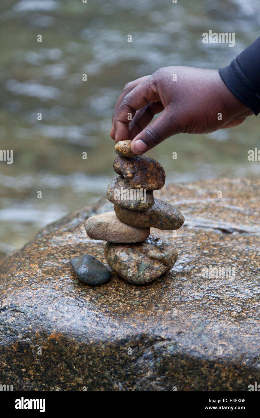 Ponendo mano pietre in una pila accanto all'acqua Foto Stock