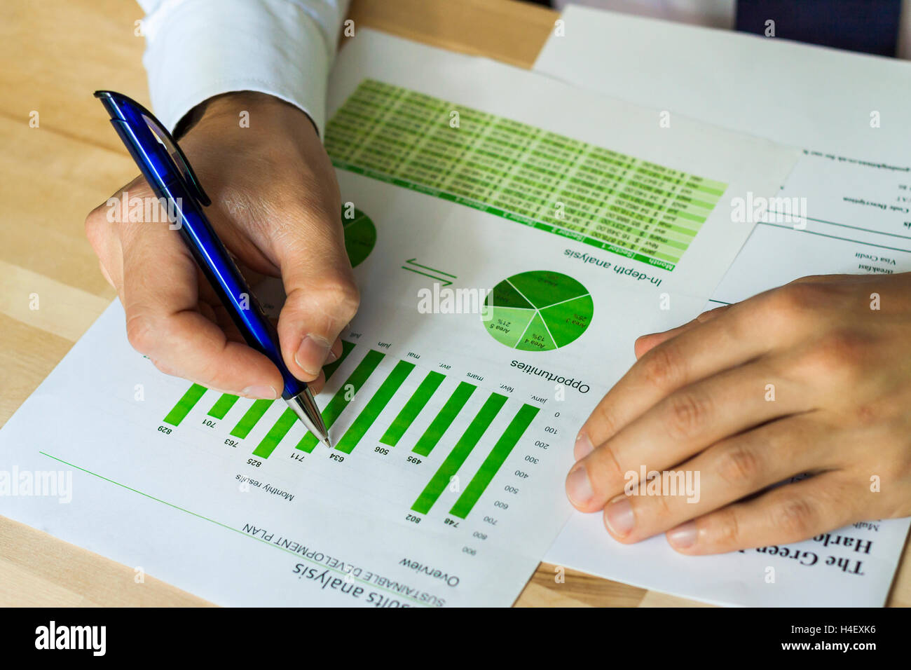 Imprenditore analizzando le opportunità di sviluppo sostenibile i grafici ad area di lavoro. Mano che tiene la penna e i grafici di verde. Foto Stock