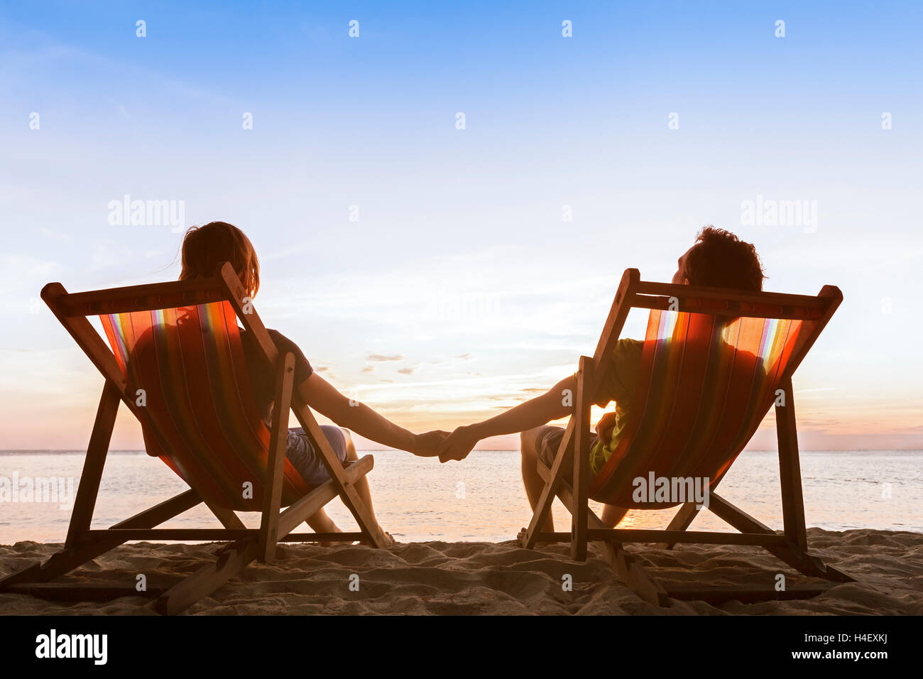 Coppia romantica seduti in sedie a sdraio sulla spiaggia godendosi la calma bellissimo tramonto Foto Stock