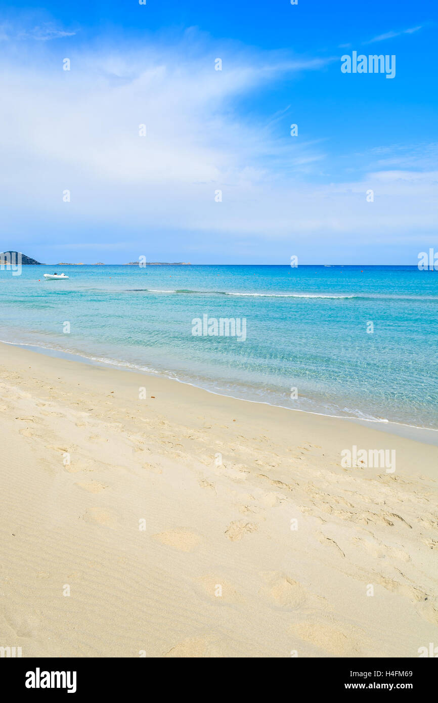 Spiaggia di sabbia bianca e la barca bianca in lontananza sul bellissimo mare turchese acqua di Porto Giunco spiaggia, l'isola di Sardegna, Italia Foto Stock