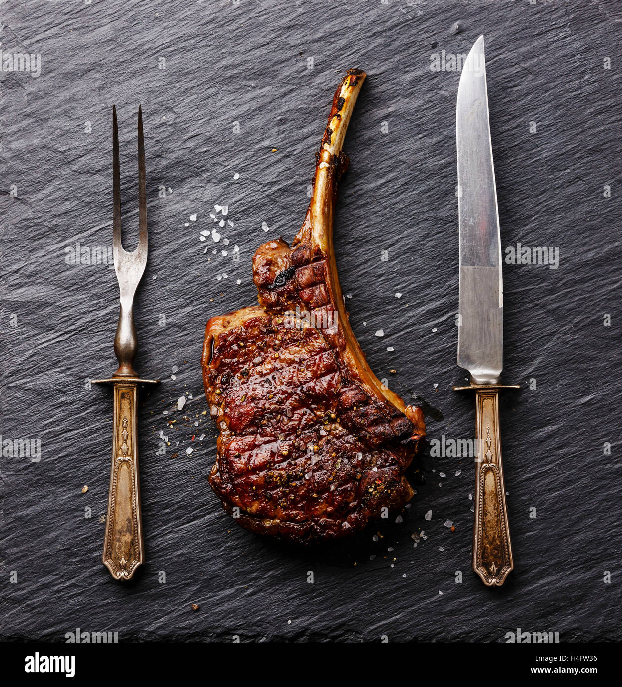 Arrosto di manzo nervatura di osso con coltello e forchetta carving impostato su nero ardesia pietra Foto Stock