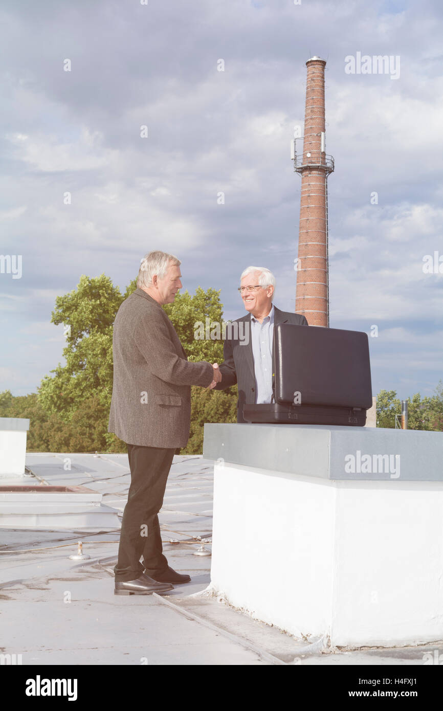 Due imprenditori senior con valigetta e di handshaking facendo un affare di lavoro all'aperto sul tetto di un edificio. Foto Stock