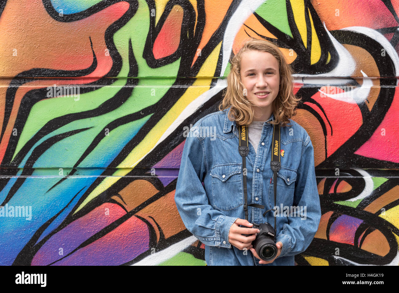 Ragazza con una telecamera in piedi contro un muro con graffiti su di esso Foto Stock