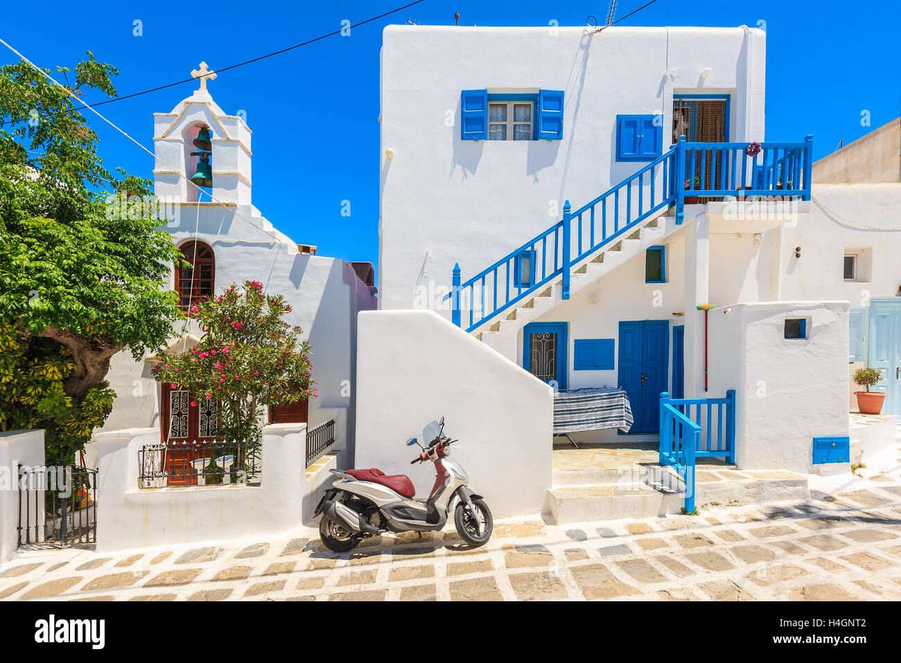 La città di Mykonos, Grecia - 16 Maggio 2016: Scooter parcheggiato su una strada di fronte a un tipico greco bianco casa e chiesa, Mykonos isla Foto Stock