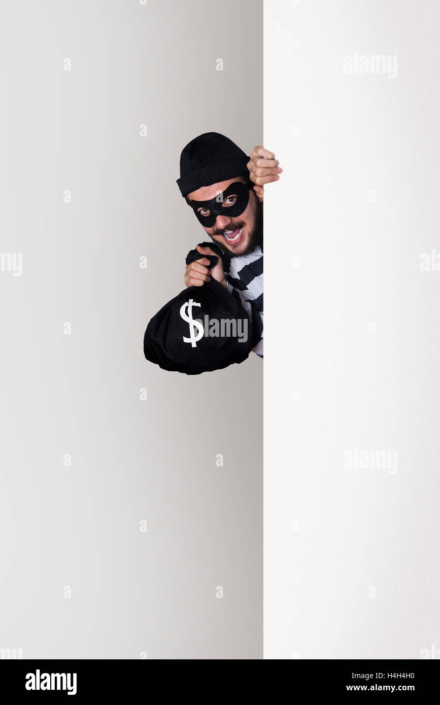 Antifurto sorridente dietro una parete con un sacco di denaro Foto Stock
