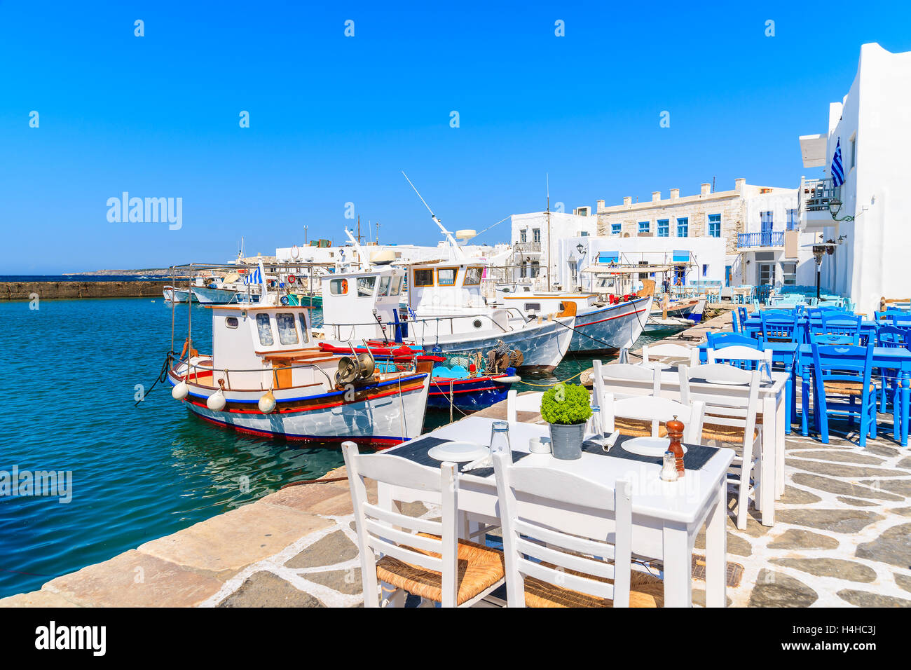 Taverna tavoli e tipico greco barche da pesca nel porto di Naoussa, isola di Paros, Cicladi Grecia Foto Stock
