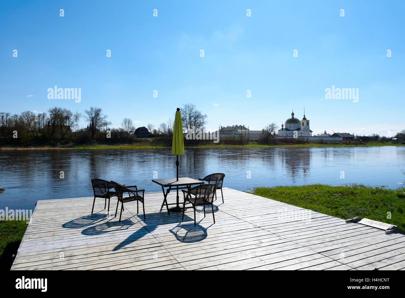 Tavolo con ombrellone su un molo in legno sulla riva del fiume contro lo sfondo dell'antico monastero Foto Stock