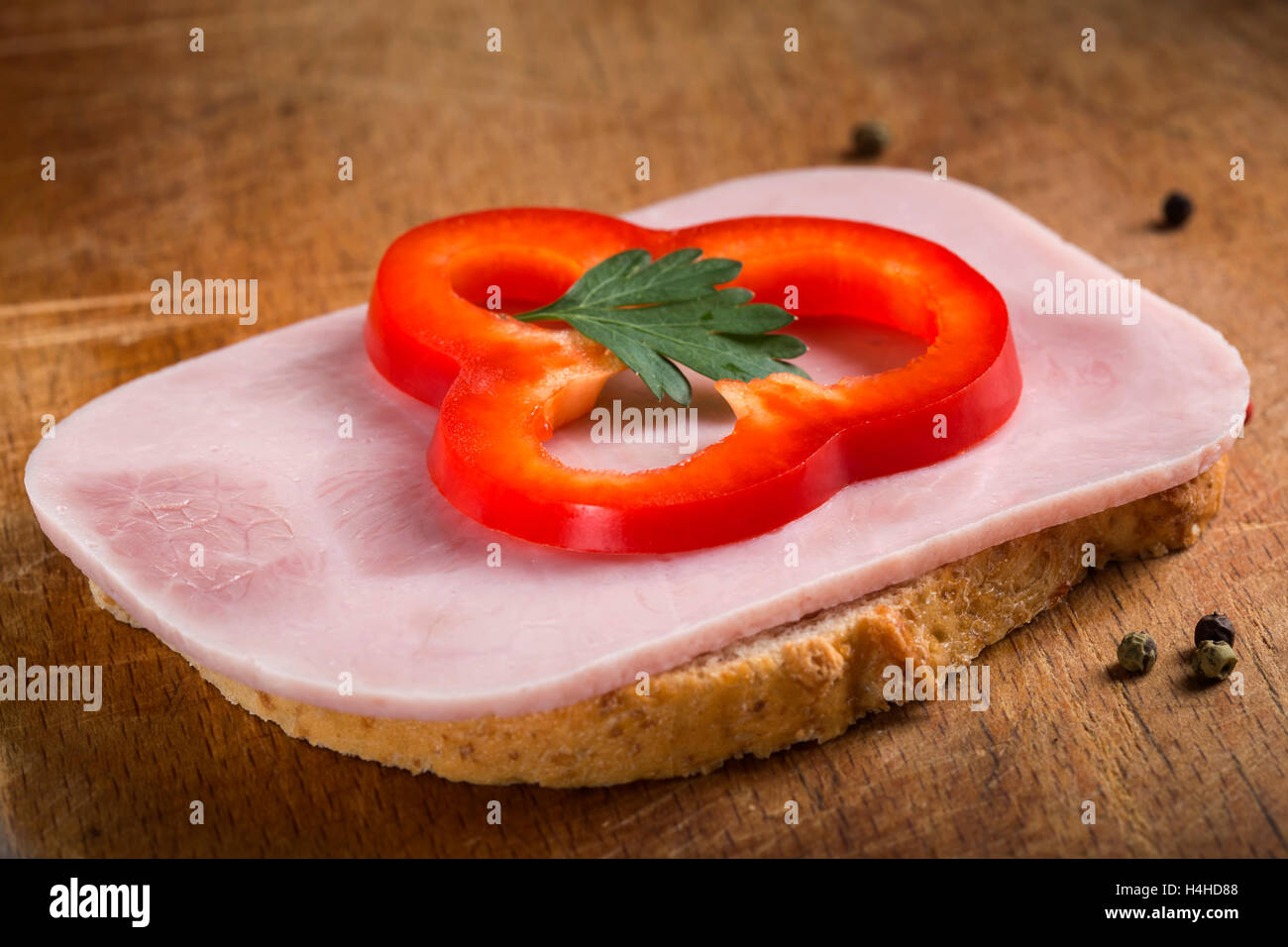 Fetta di pane con prosciutto crudo fresco e pepe rosso su sfondo di legno Foto Stock