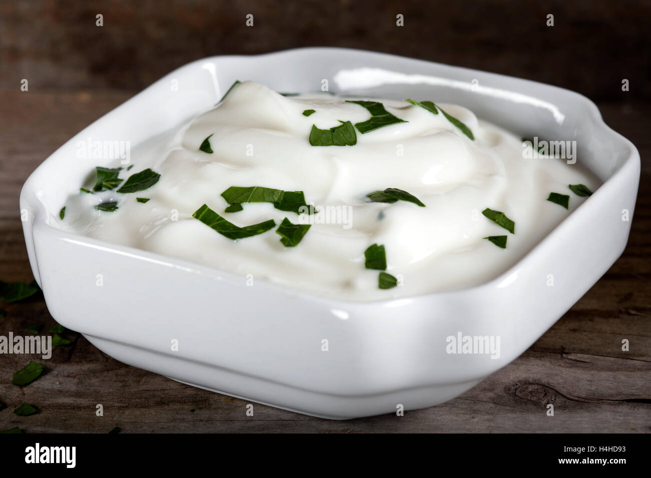 Ciotola di panna acida o yogurt con le erbe in un vaso bianco su sfondo di legno Foto Stock