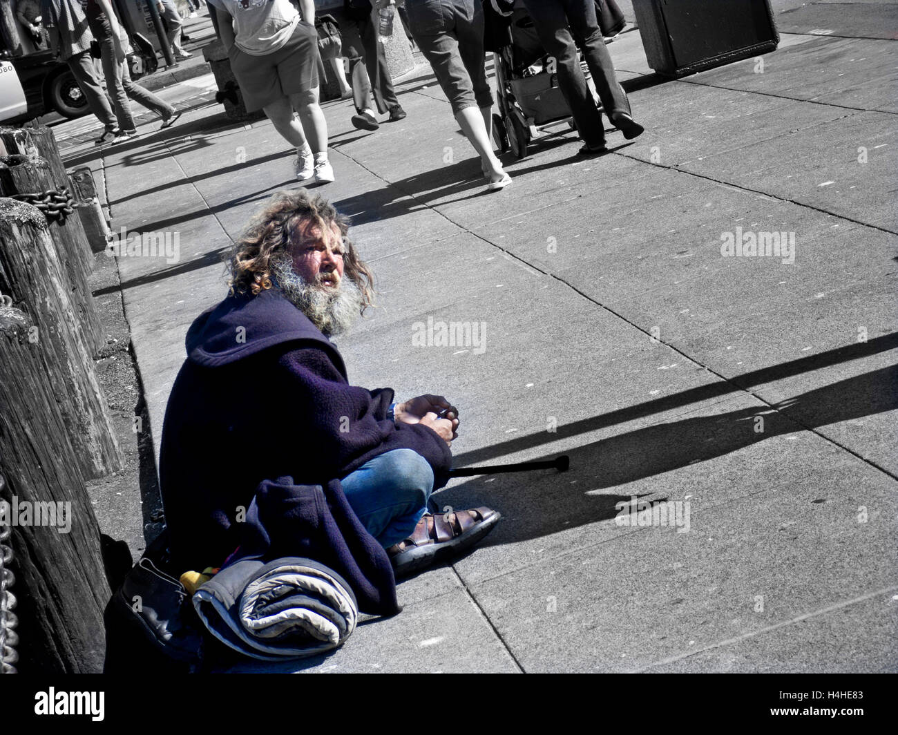 Senzatetto disabilitato l uomo di accattonaggio sul marciapiede della città con persone di passaggio (parziale B&W trattamento concettuale) Foto Stock