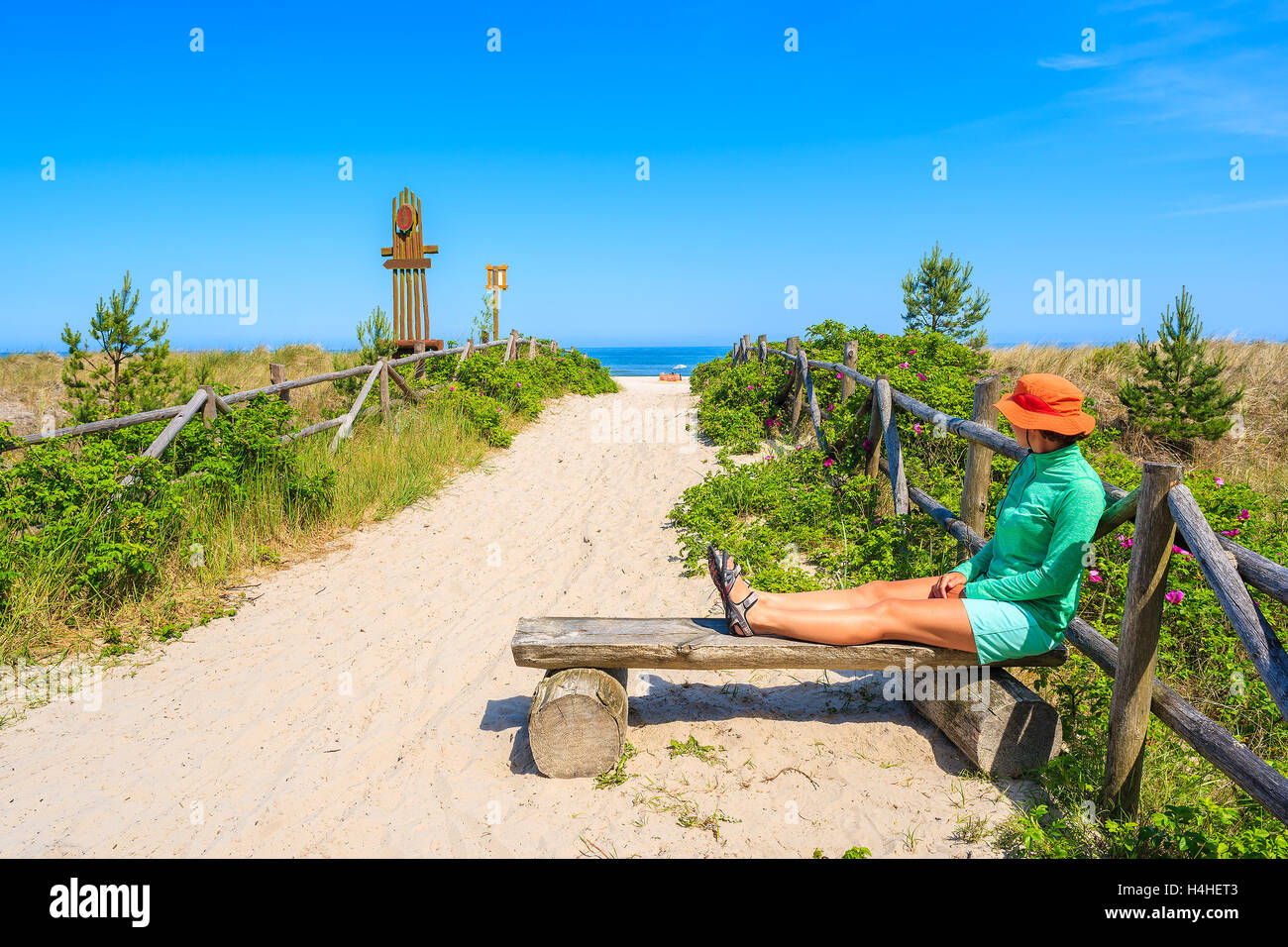 Giovane donna seduta turistica sul banco di lavoro in entrata a una bellissima spiaggia di sabbia in Lubiatowo villaggio costiero, Mar Baltico, Polonia Foto Stock
