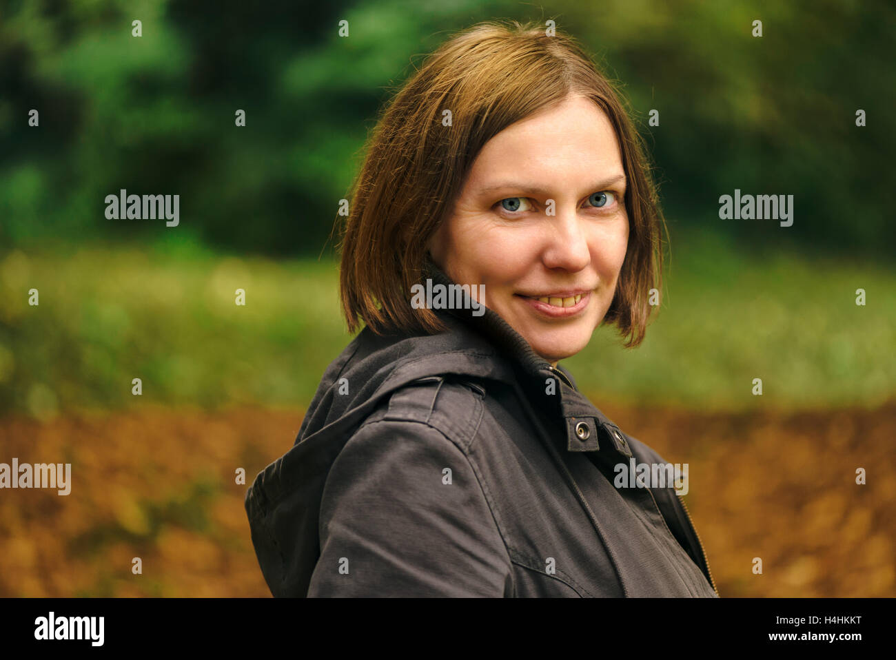 Bella sorridente giovane adulto donna gentile che pongono in autunno park e guardando la fotocamera Foto Stock