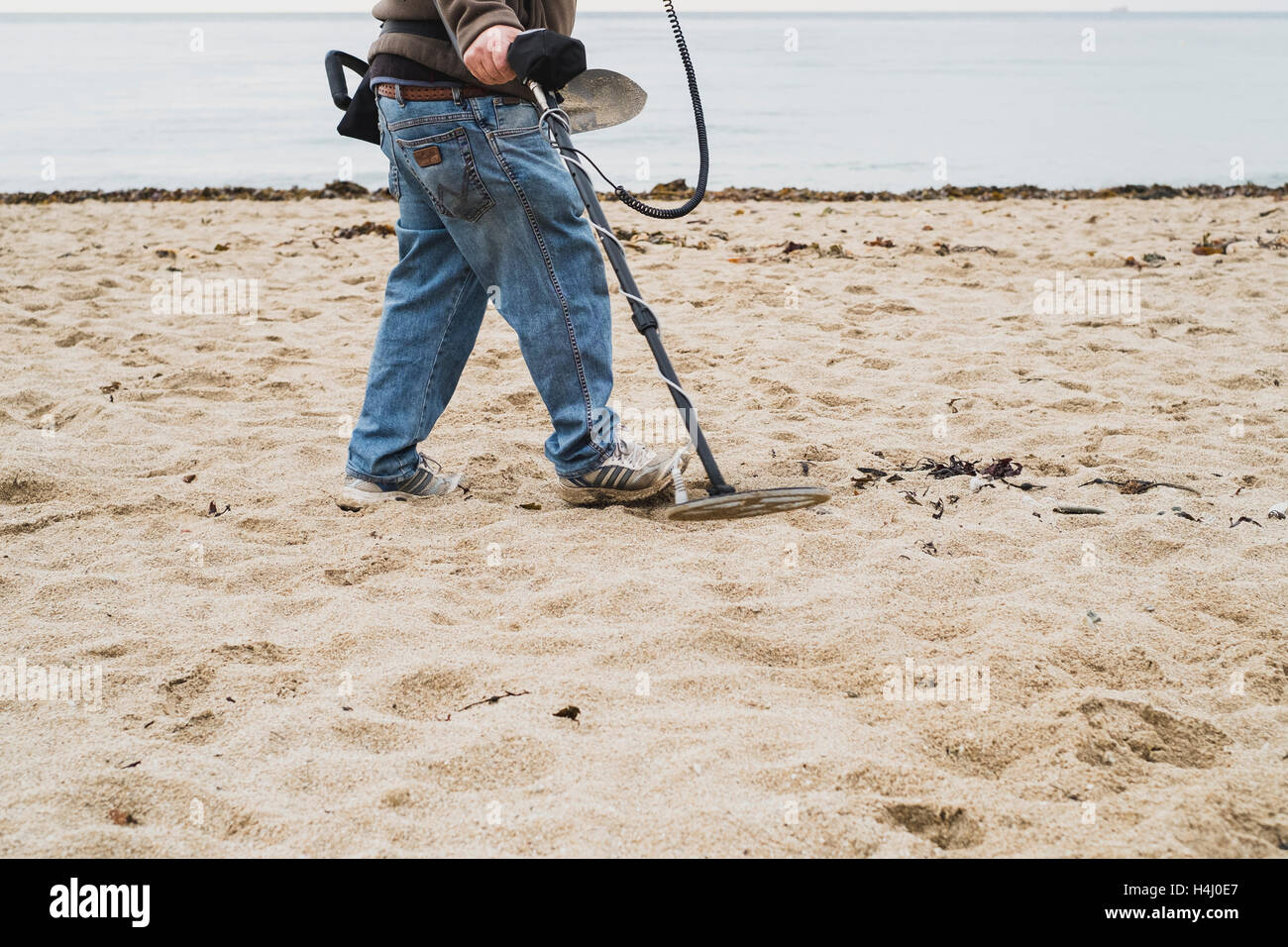 Un uomo con un rivelatore di metallo lavorando su Falmouth's Gyllyngvase Beach Foto Stock