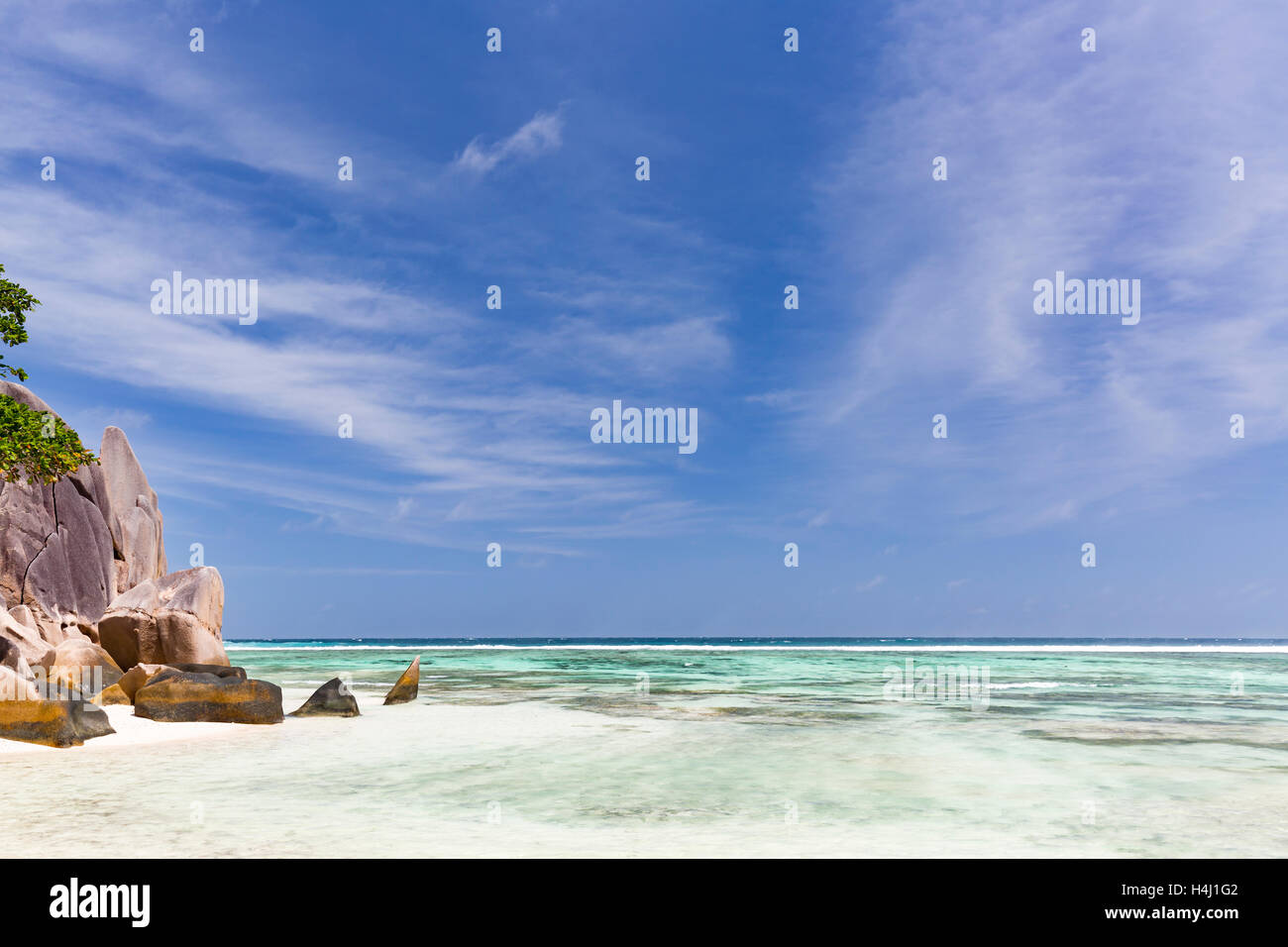 Laguna turchese con coralli vicino a una splendida spiaggia di sabbia bianca con scenic rocce granitiche e cielo blu Foto Stock