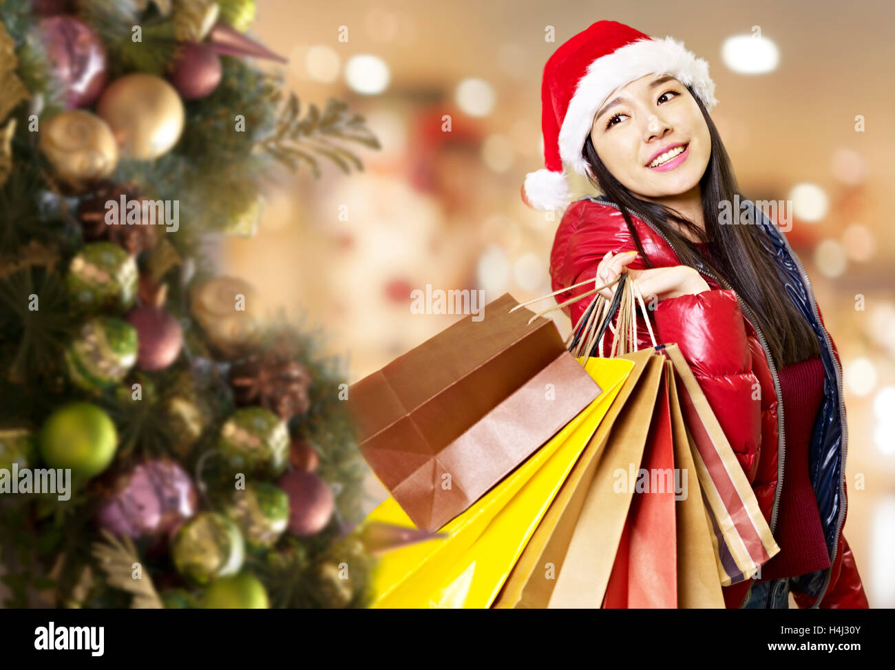Giovane donna asiatica che trasportano i sacchi di carta sulla spalla durante lo shopping natalizio, felice e sorridente. Foto Stock