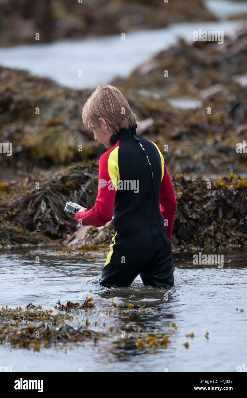 Ragazzo guadare attraverso rock pool con telecamera di azione Foto Stock