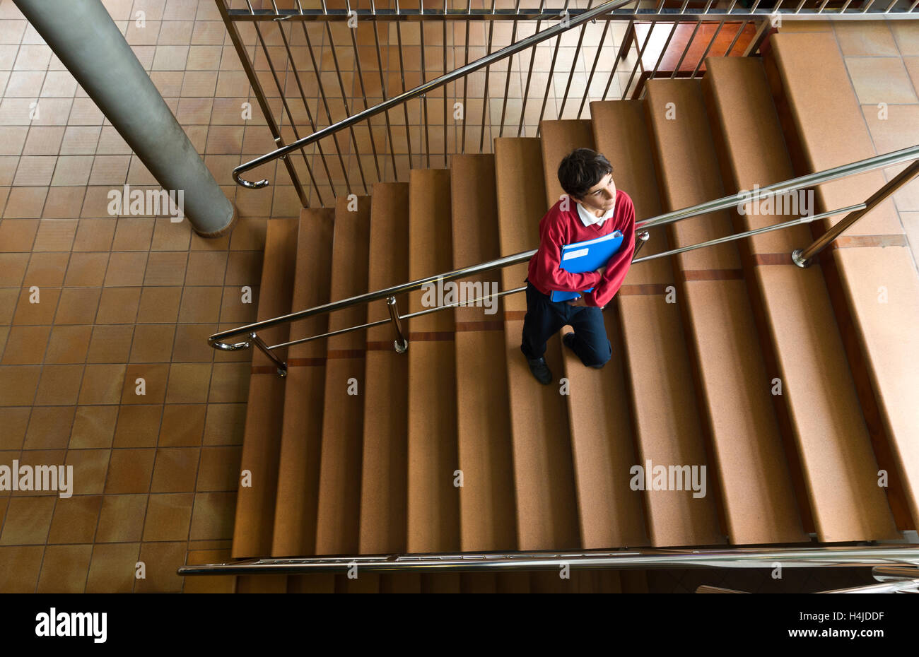 Malinconici Junior scolaro con cartella in aula in attesa solo nella tromba delle scale della scuola Foto Stock