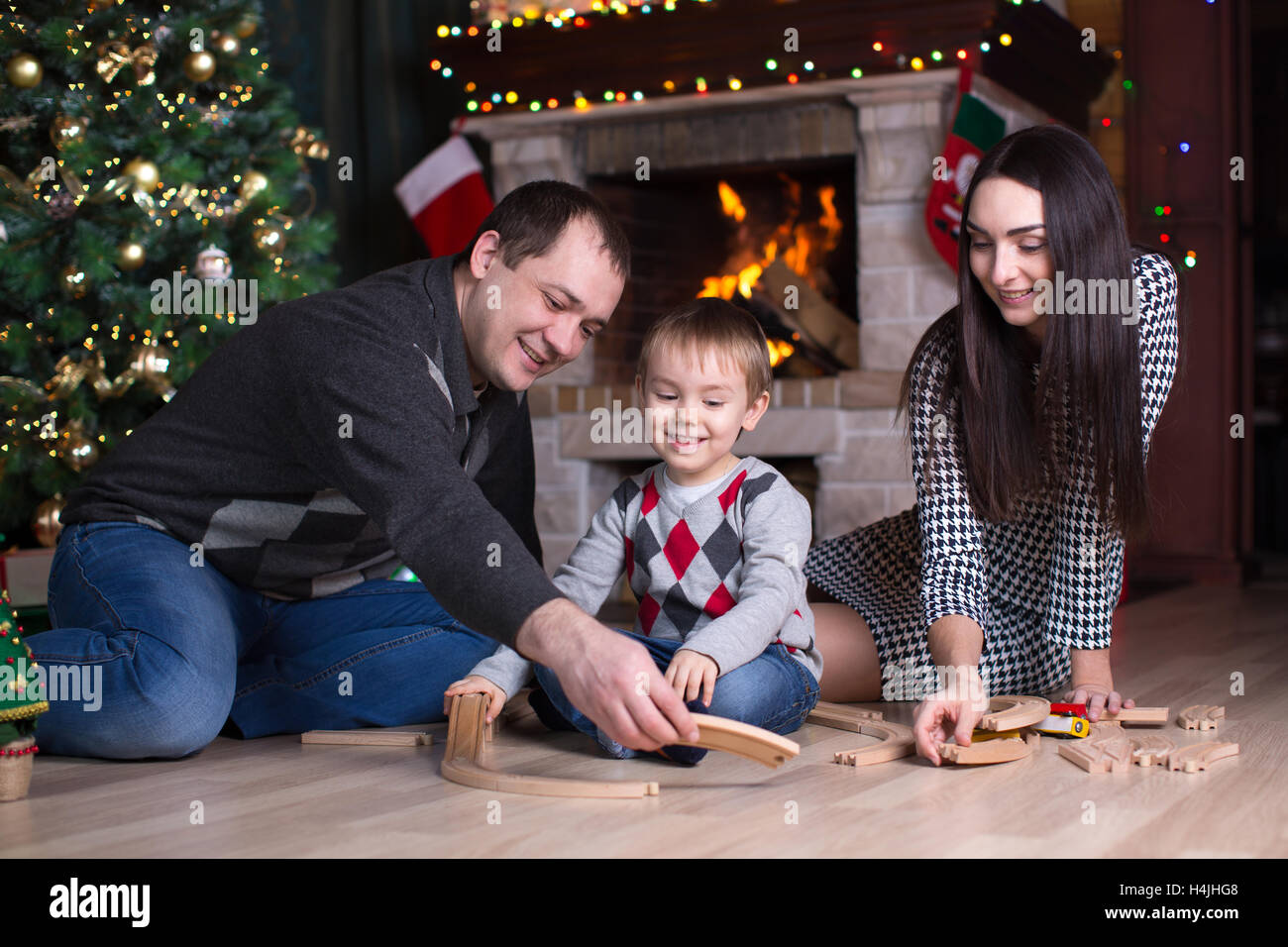 I genitori e il loro figlio giocare con modello ferroviario nei pressi di albero di natale in camera Foto Stock