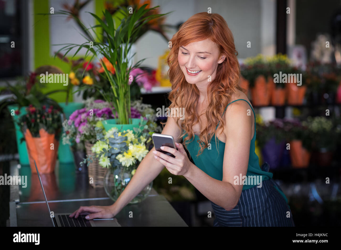 Fiorista femmina tramite telefono cellulare durante l'utilizzo di laptop Foto Stock