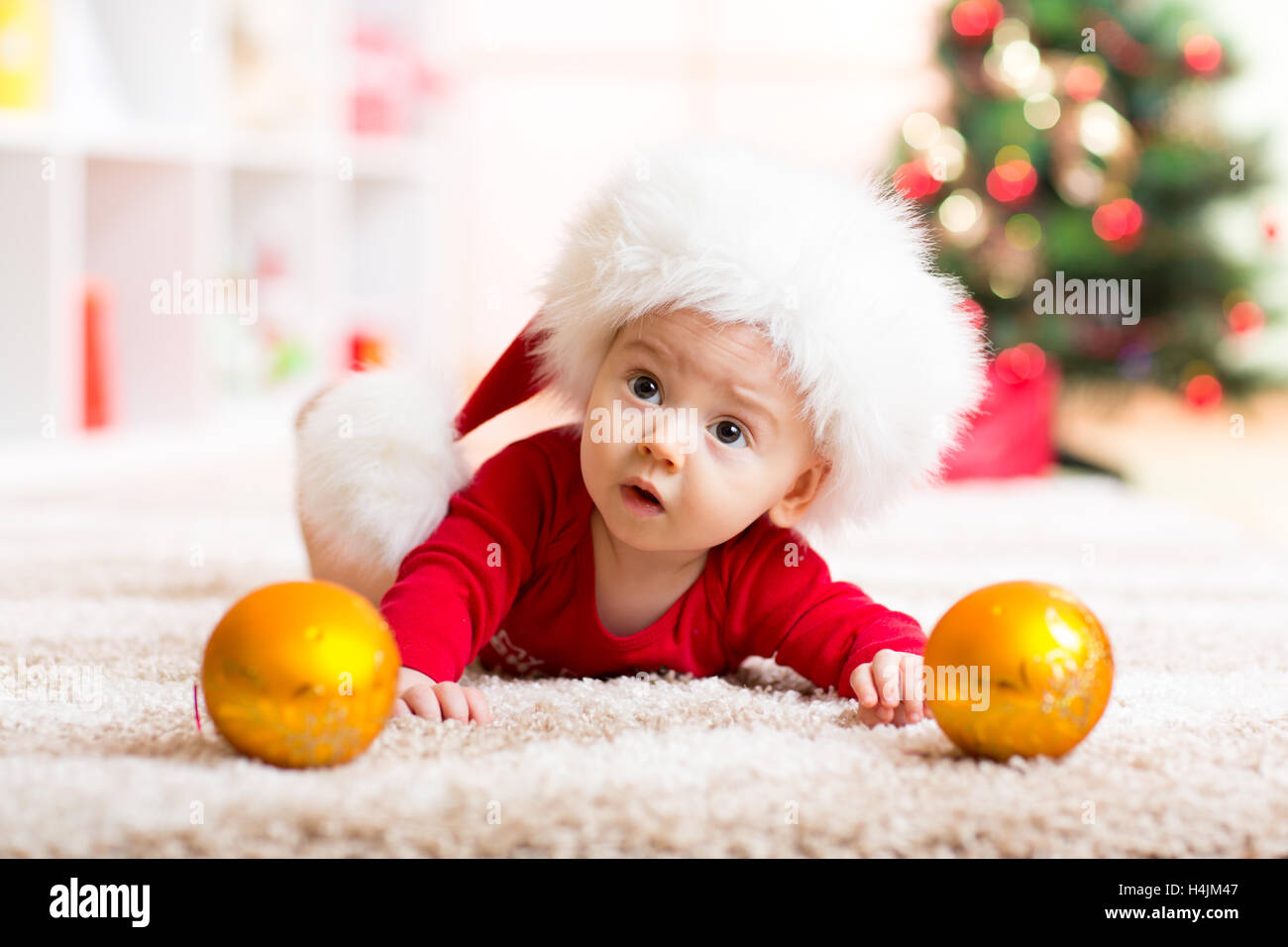 Funny baby giacente sulla pancia indossando Santa hat e tuta nella parte anteriore dell albero di Natale Foto Stock