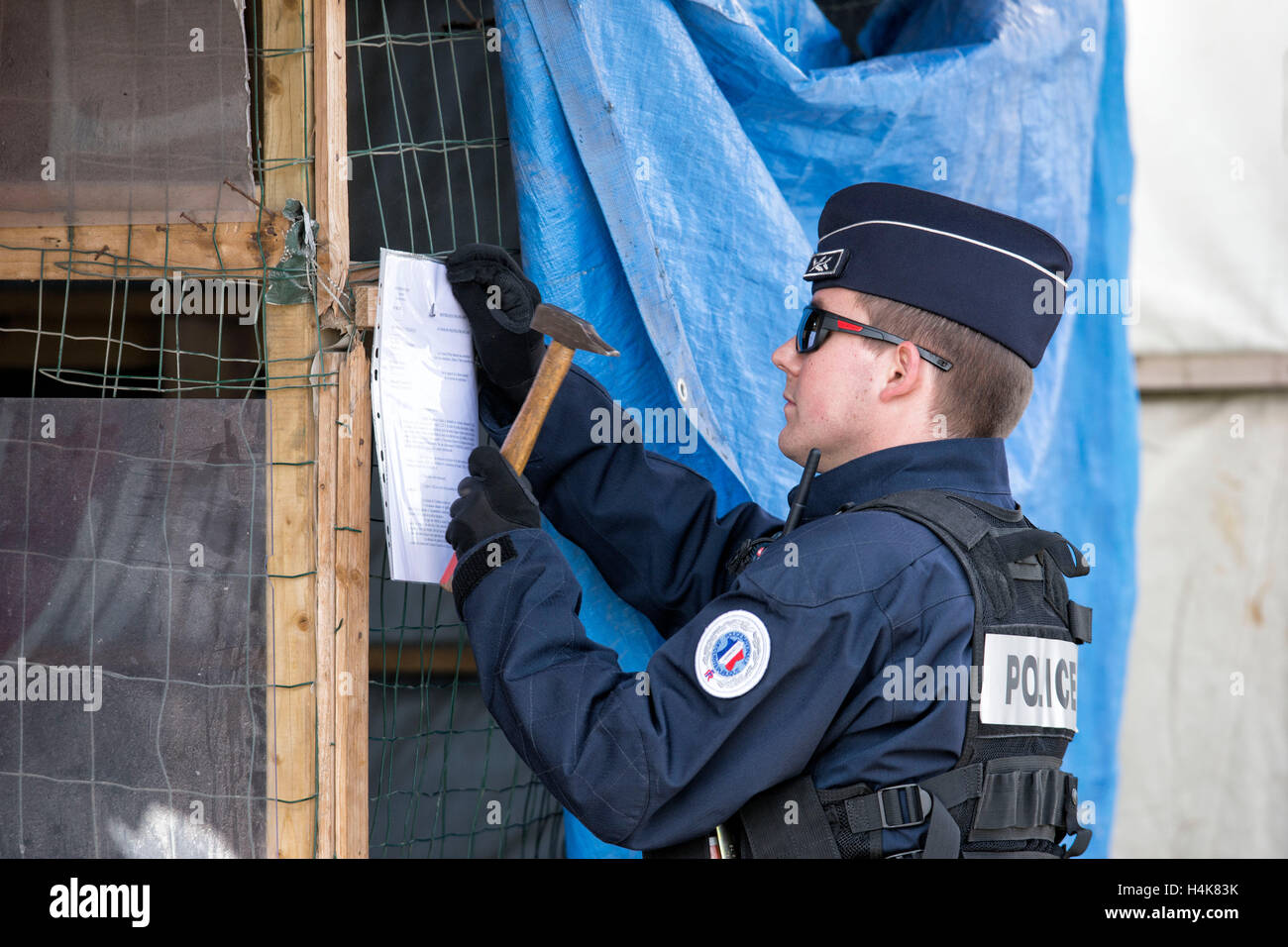 Calais, Francia. Xvii oct, 2016. Un francese di funzionario di polizia chiodi un avviso di sfratto per una delle capanne, prima del previsto la demolizione del 'Calais giungla' campo di migranti a Calais, Francia, 17 ottobre 2016. Per anni, i migranti che cercano di entrare clandestinamente nel Regno Unito si sono riuniti nel camp mediante il canale inglese. Foto: ARNULF STOFFEL/DPA - nessun filo SERVICE - © dpa/Alamy Live News Foto Stock
