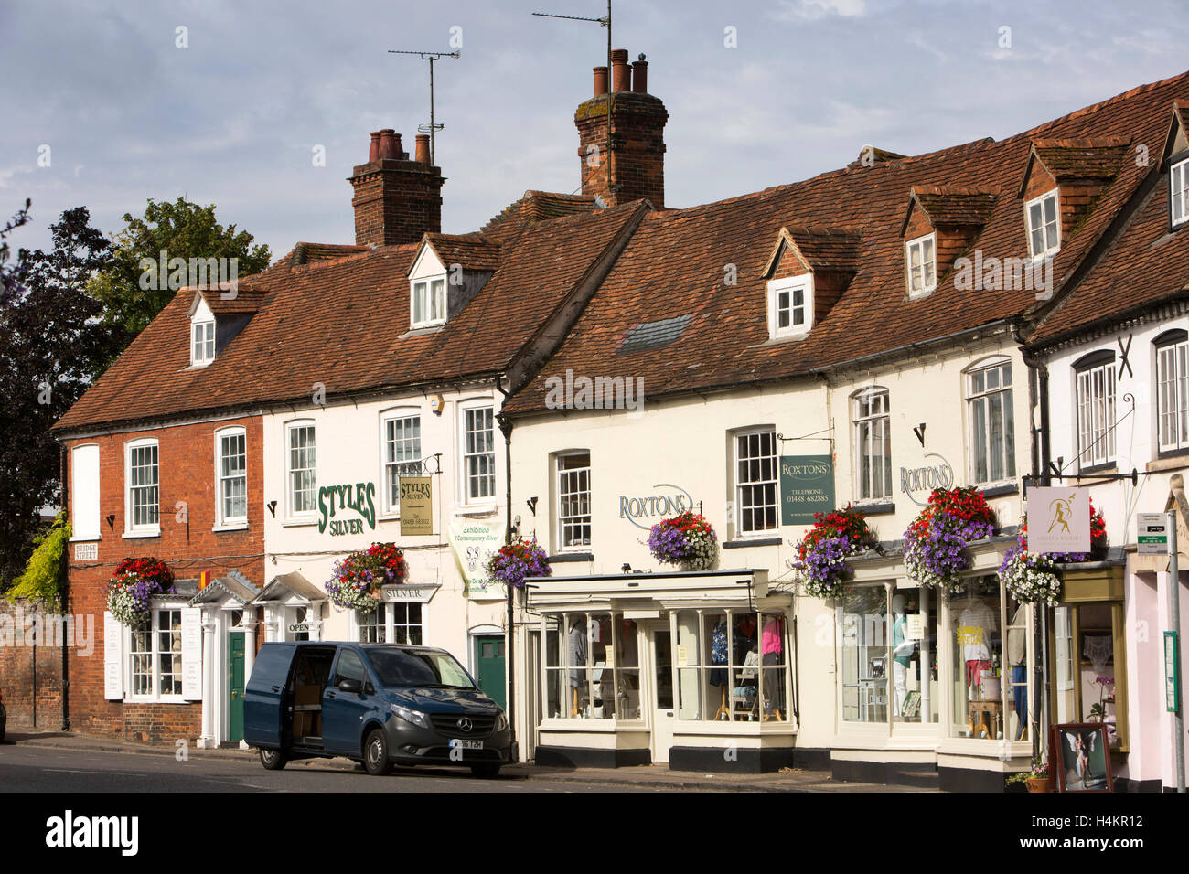 Inghilterra, Berkshire, Hungerford, Bridge Street, motivi floreali colorati nei cestini appesi su negozi di antiquariato Foto Stock