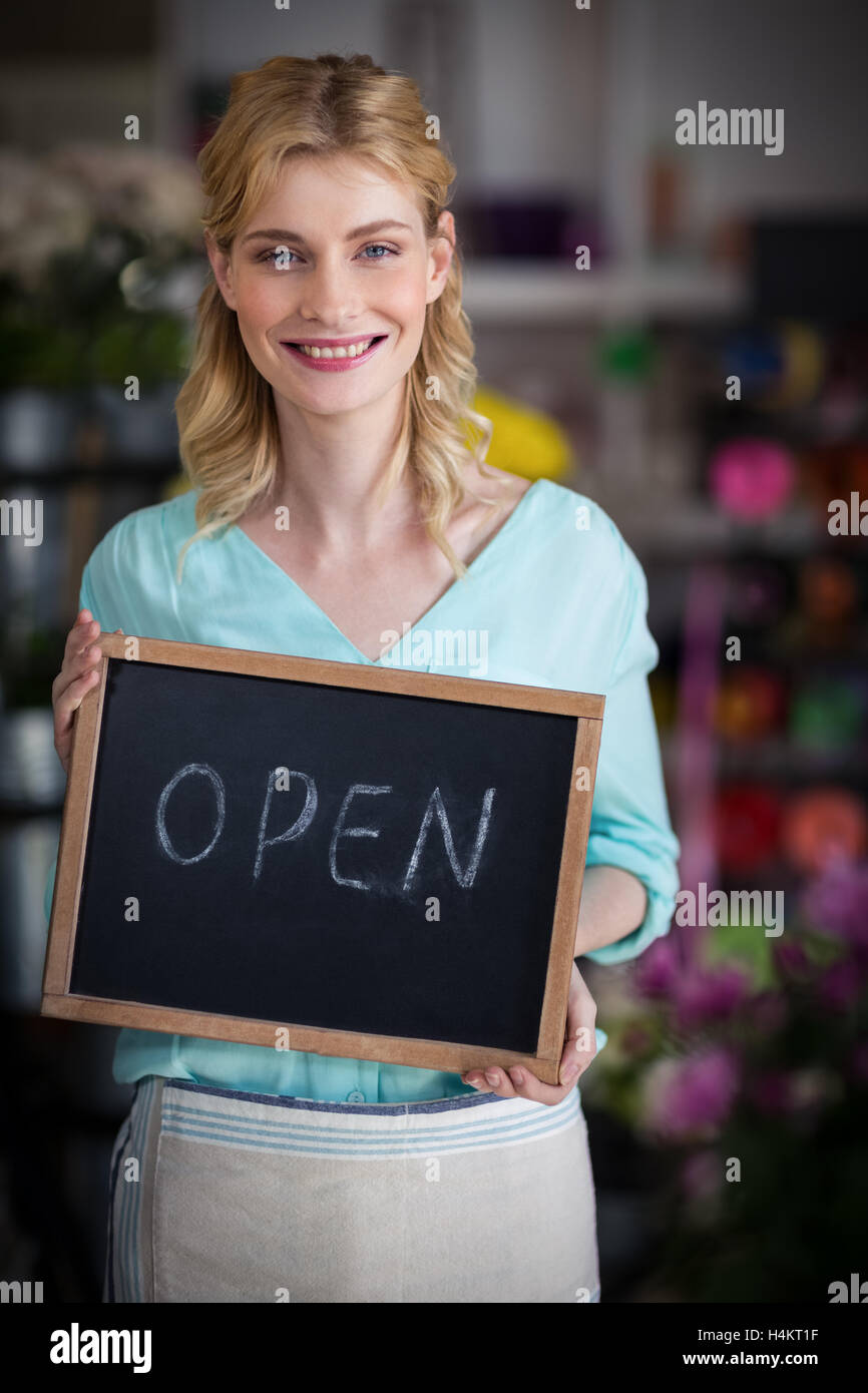 Donna sorridente fioraio tenendo aperte segno su ardesia in negozio di fiori Foto Stock