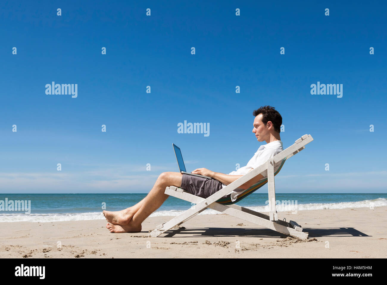 Felice giovani freelance che lavorano online con il computer portatile su una soleggiata spiaggia tropicale Foto Stock