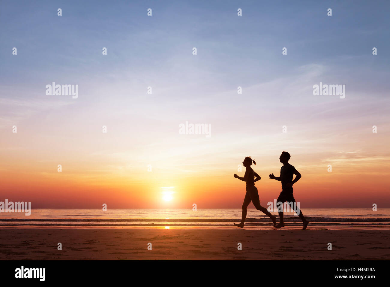 Silhouette di due guide sportive in esecuzione sulla spiaggia al tramonto, concetto su uno stile di vita sano e benessere Foto Stock