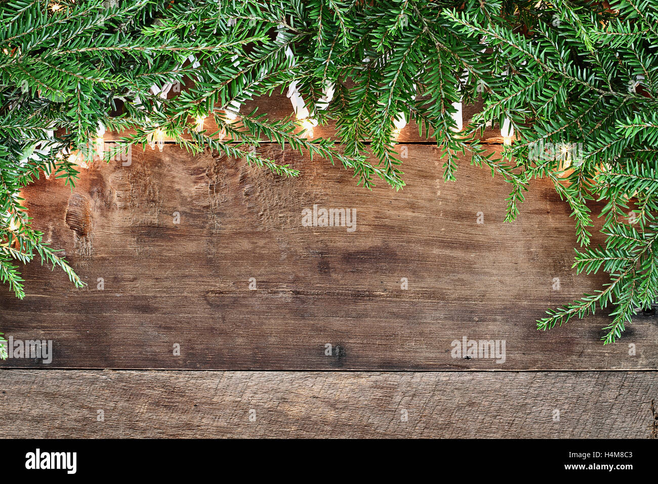 Albero di natale di rami di pino e luci decorative su un sfondo rustico di legno del granaio. Immagine ripresa dalla testa. Foto Stock