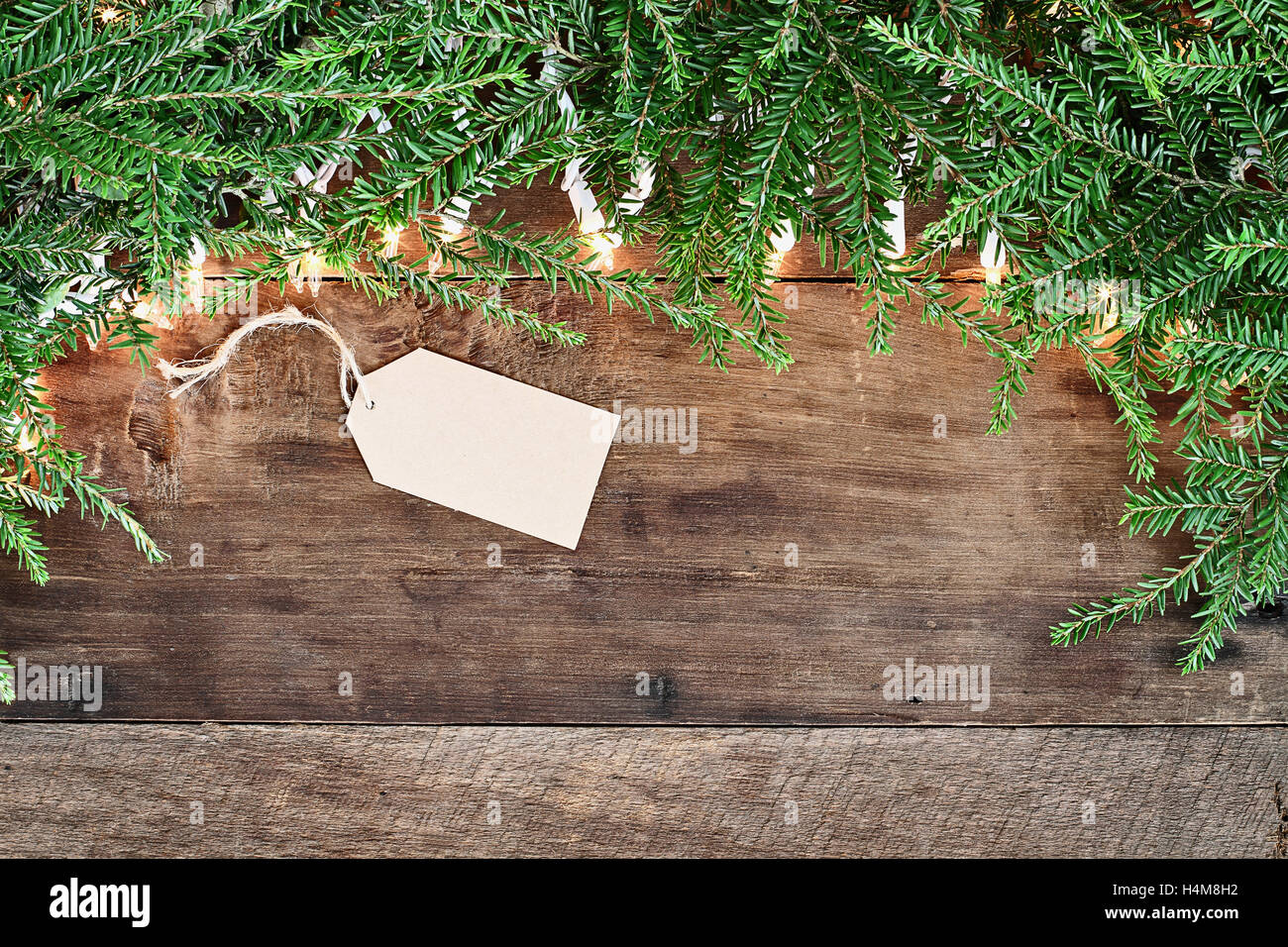 Albero di natale rami di pino, la scheda vuota e luci decorative su un sfondo rustico di legno del granaio. Immagine ripresa dalla testa. Foto Stock