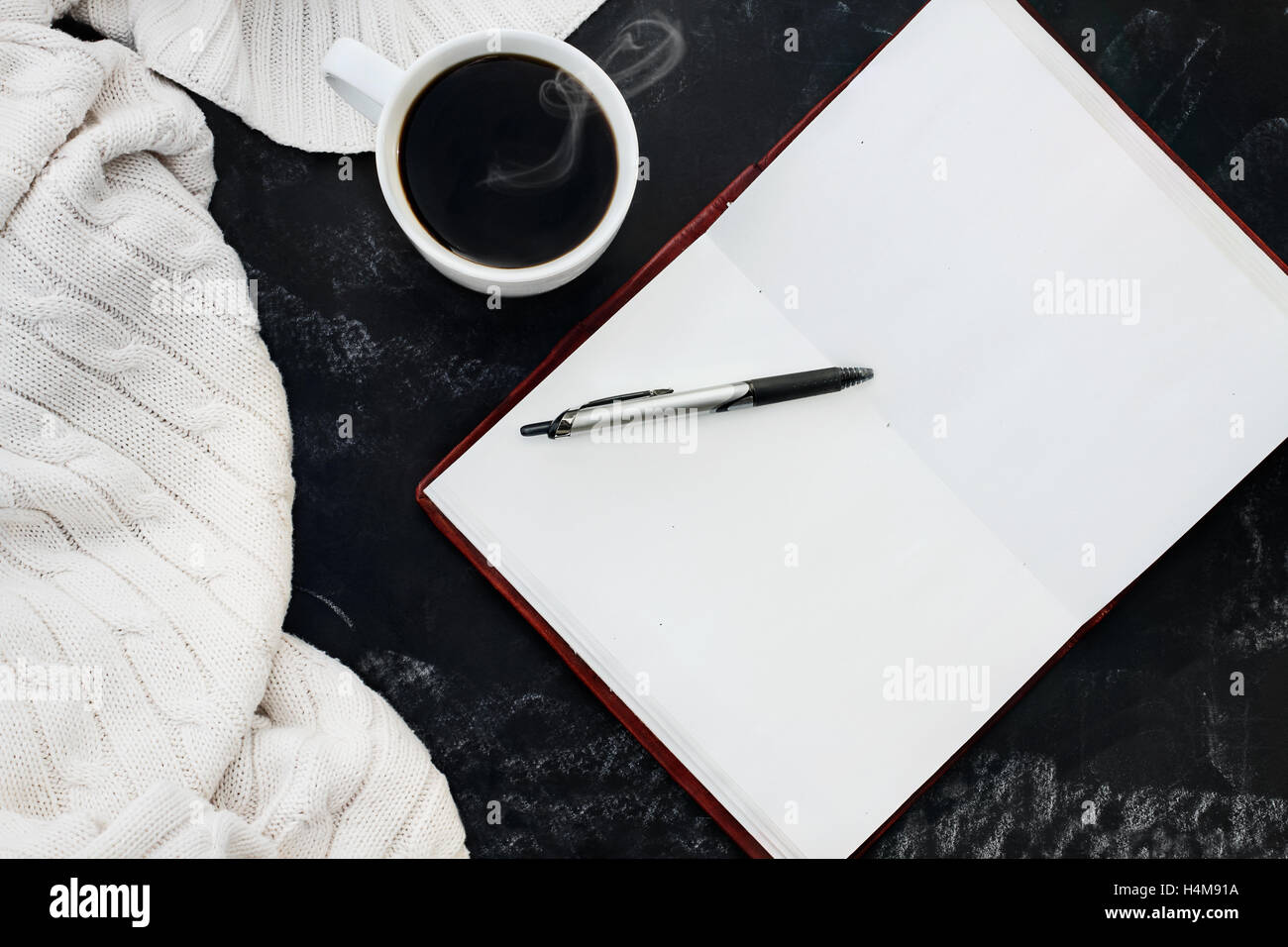 Morbido maglione maglia coperta con una tazza di caffè caldo e un libro aperto con la penna sulla lavagna grungy sfondo. Foto Stock
