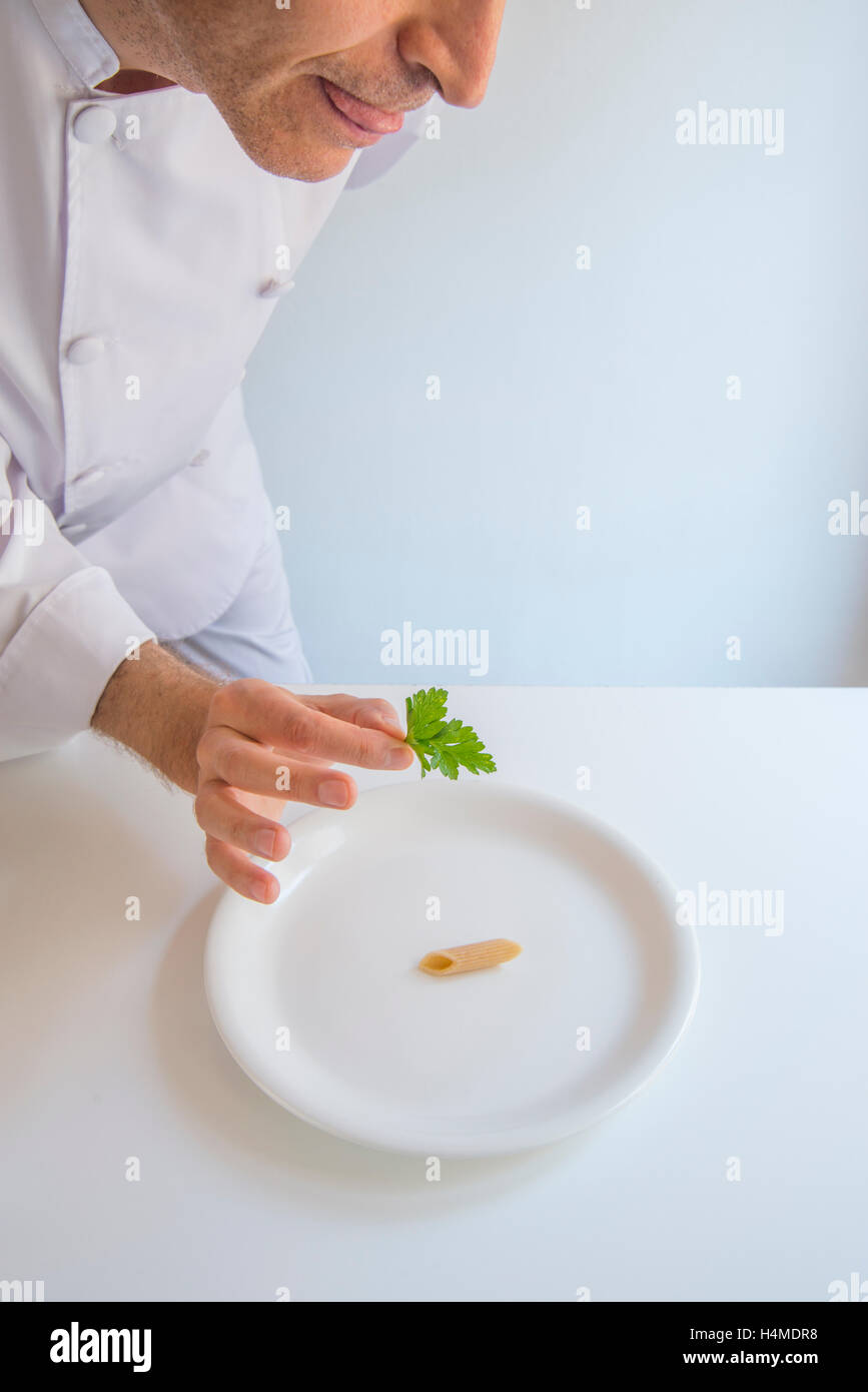 La nouvelle cuisine: minimalismo. Umoristico. Lo Chef mettendo una foglia di prezzemolo sulla parte superiore di un singolo maccheroni. Foto Stock