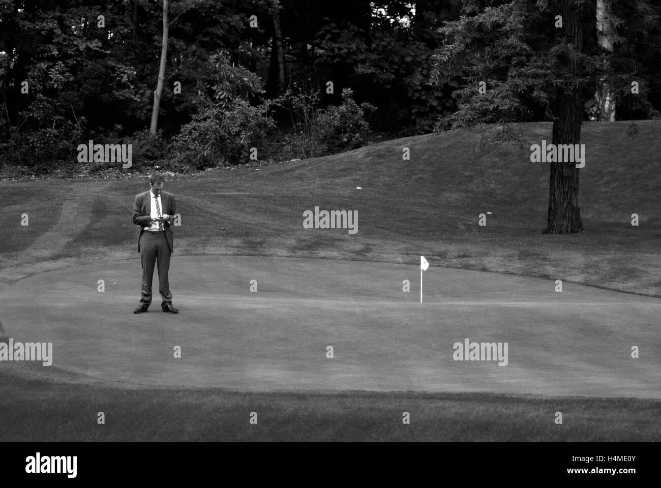 Imprenditore texting sul golf green / Uomo in tuta sul campo da golf Foto Stock
